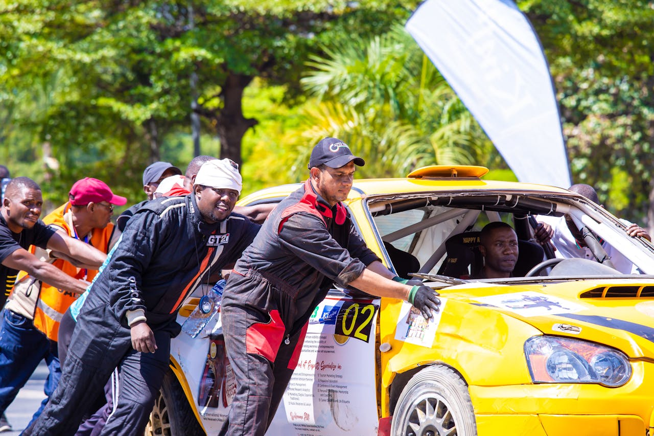 Group of men collaborating to push a car during an outdoor racing event.
